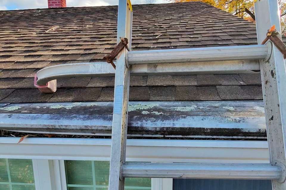 A ladder set up at a house’s roofline for gutter work.
